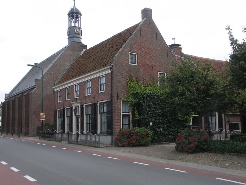 Oud herenhuis met klimop en hortensia's naast de dorpskerk met torentje in Elst