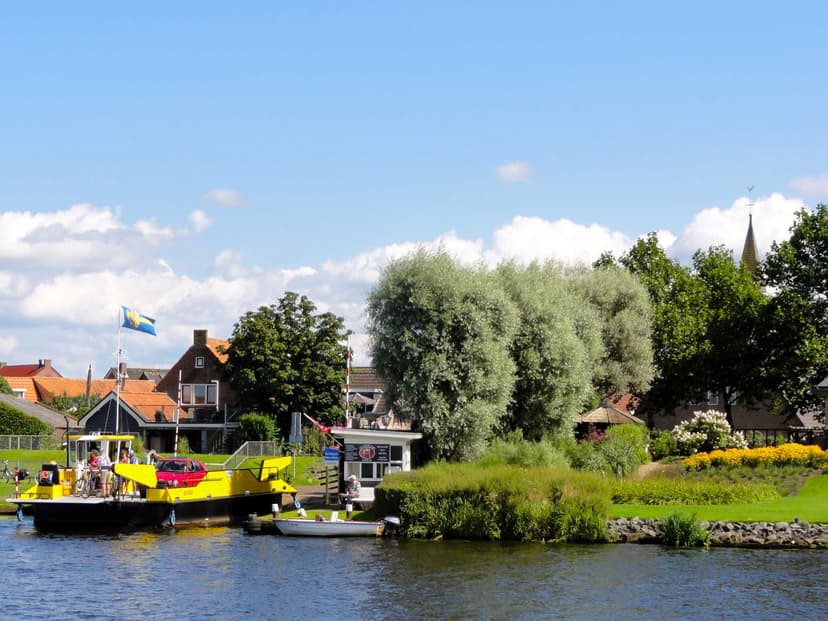 Het gele pontje over de Eem bij Eemdijk, met huizen en de kerktoren erachter