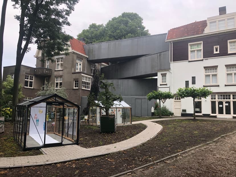 Tuin van het Nationaal Glasmuseum in Leerdam, met glazen kassen en de grijze loopbrug tussen de villa's